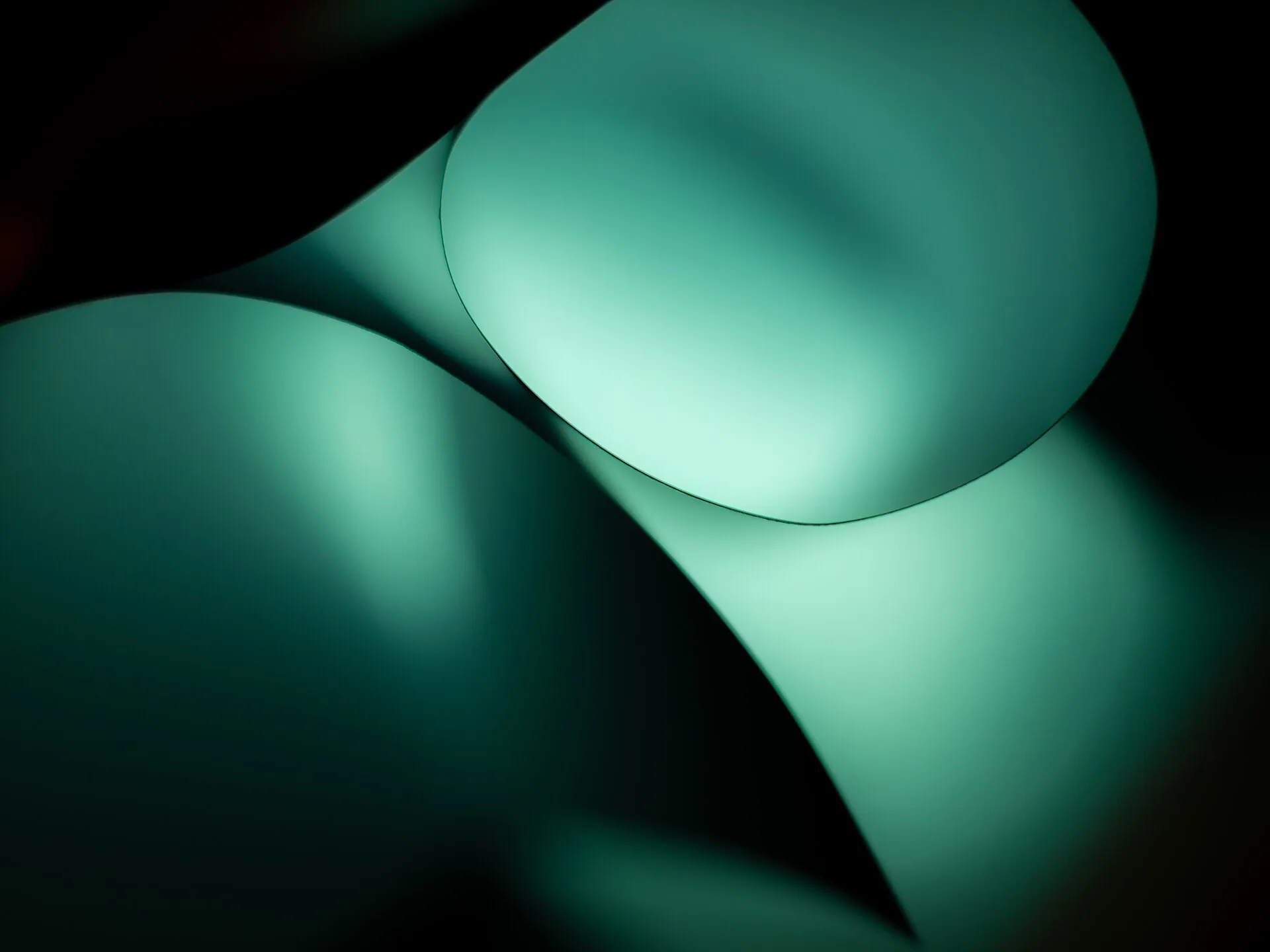 Curved sheets of paper lit in teal against black
