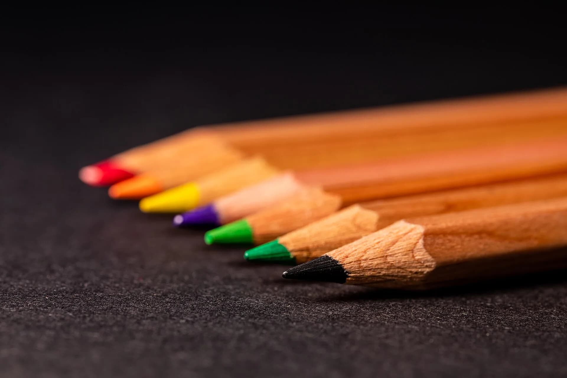 Row of coloured pencil tips on a dark surface
