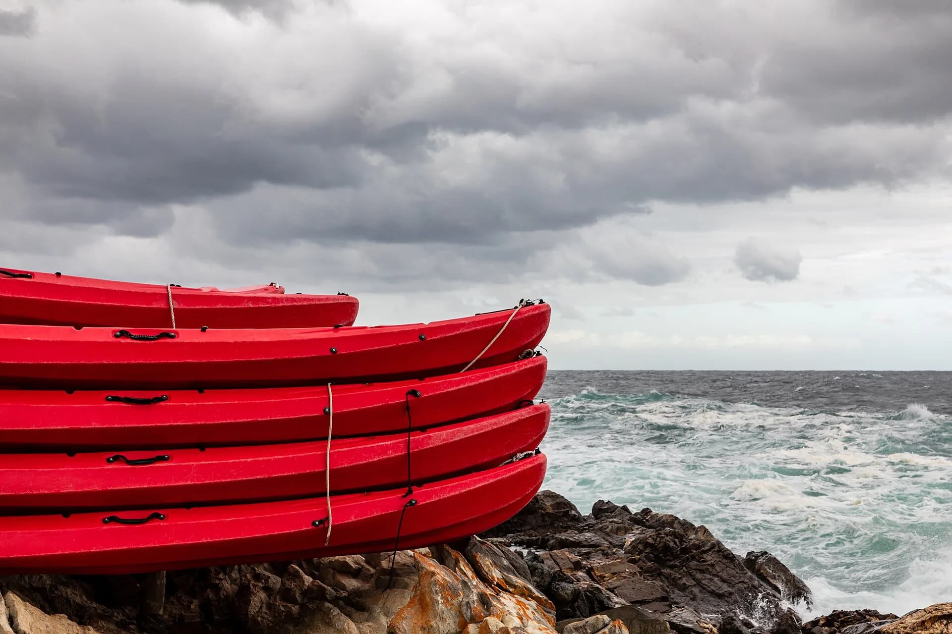 Stacked red kayaks on rocks beside a stormy sea