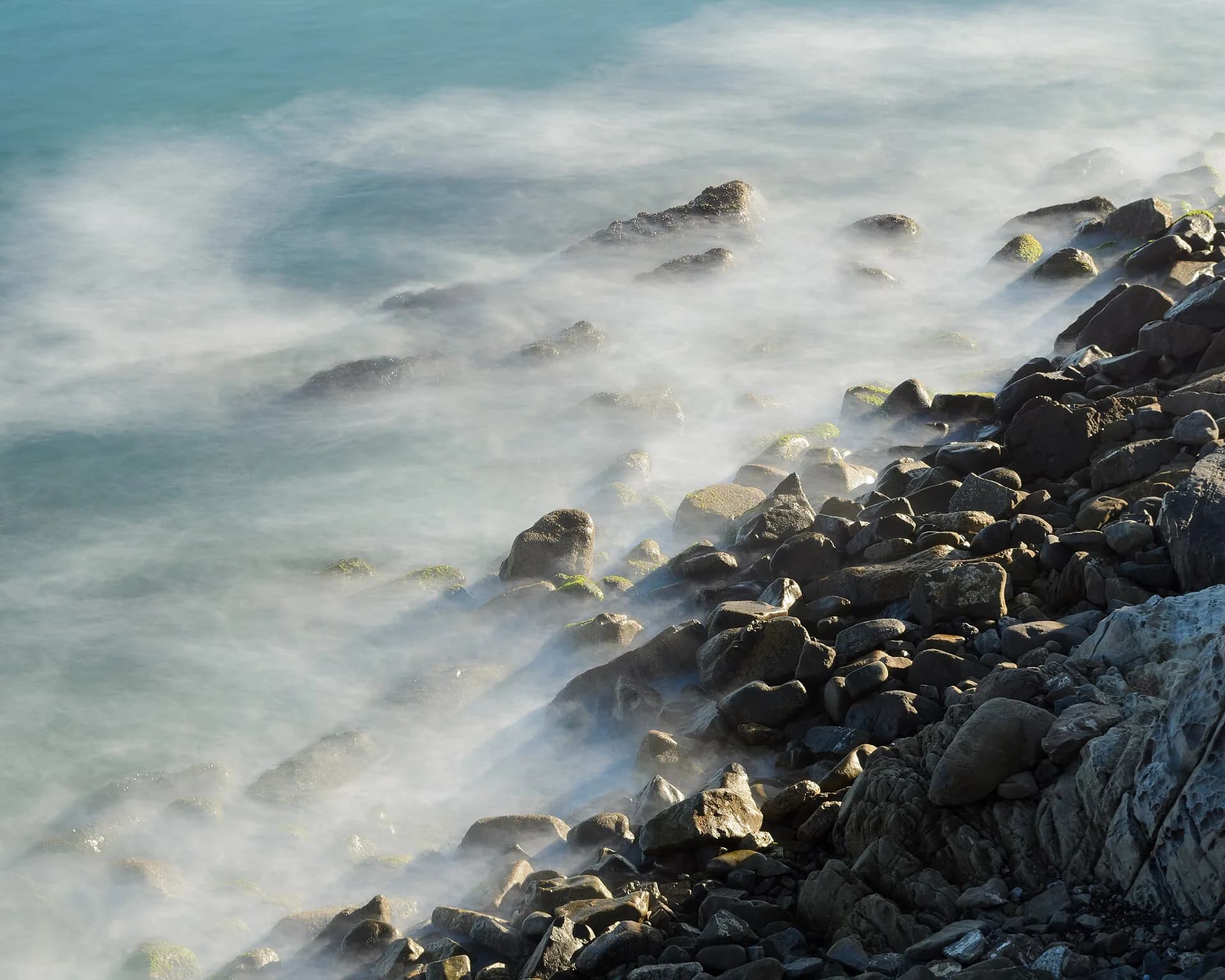 Long-exposure waves washing over dark coastal rocks
