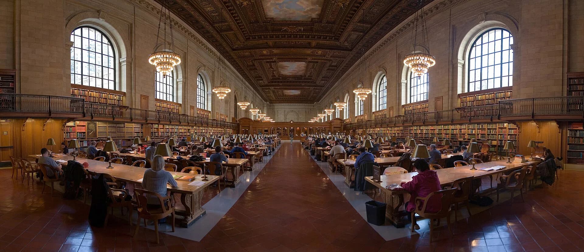 Long reading room with tables and arched windows