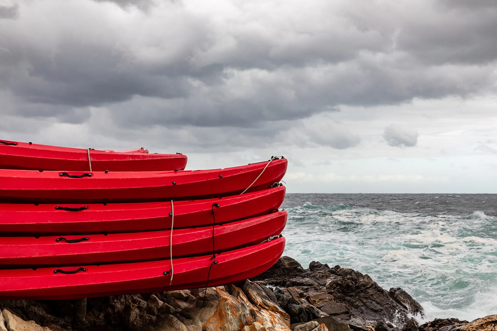 Stacked red kayaks on rocks beside a stormy sea